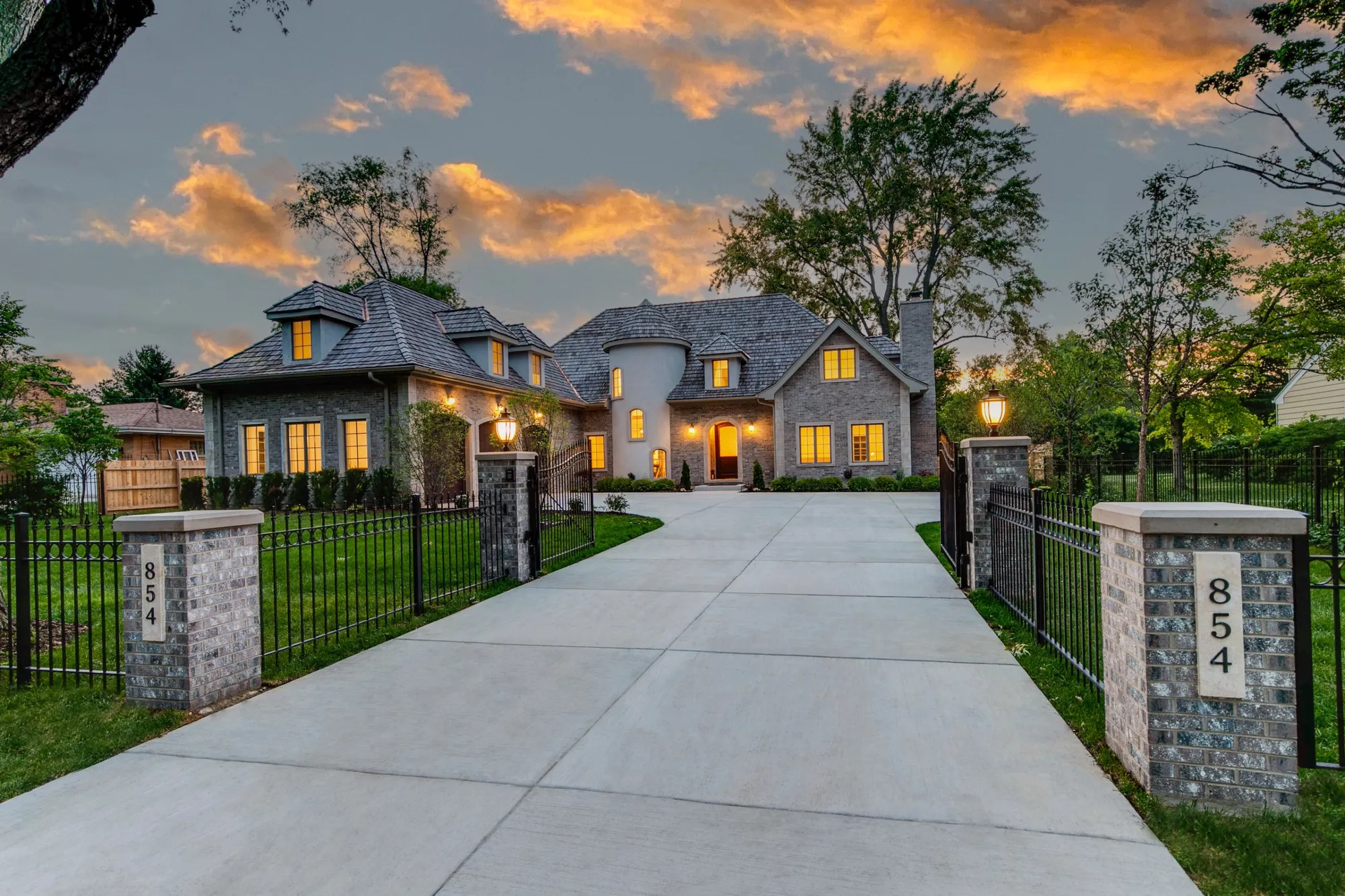 Gated stone entrance at dusk, pillars marked 854 glowing like lanterns