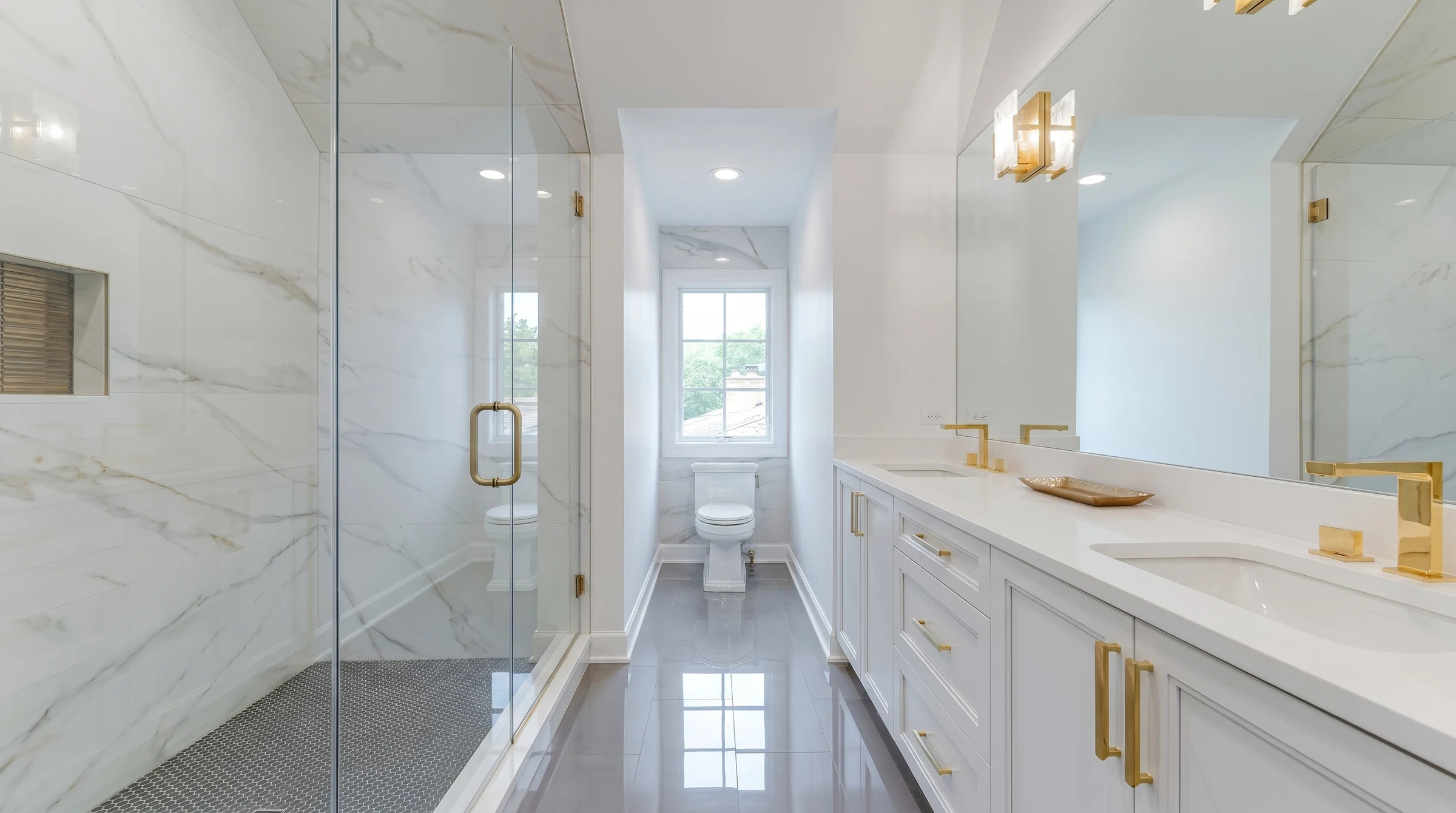 Guest bath with book-matched marble, a glass shower and twin vanities