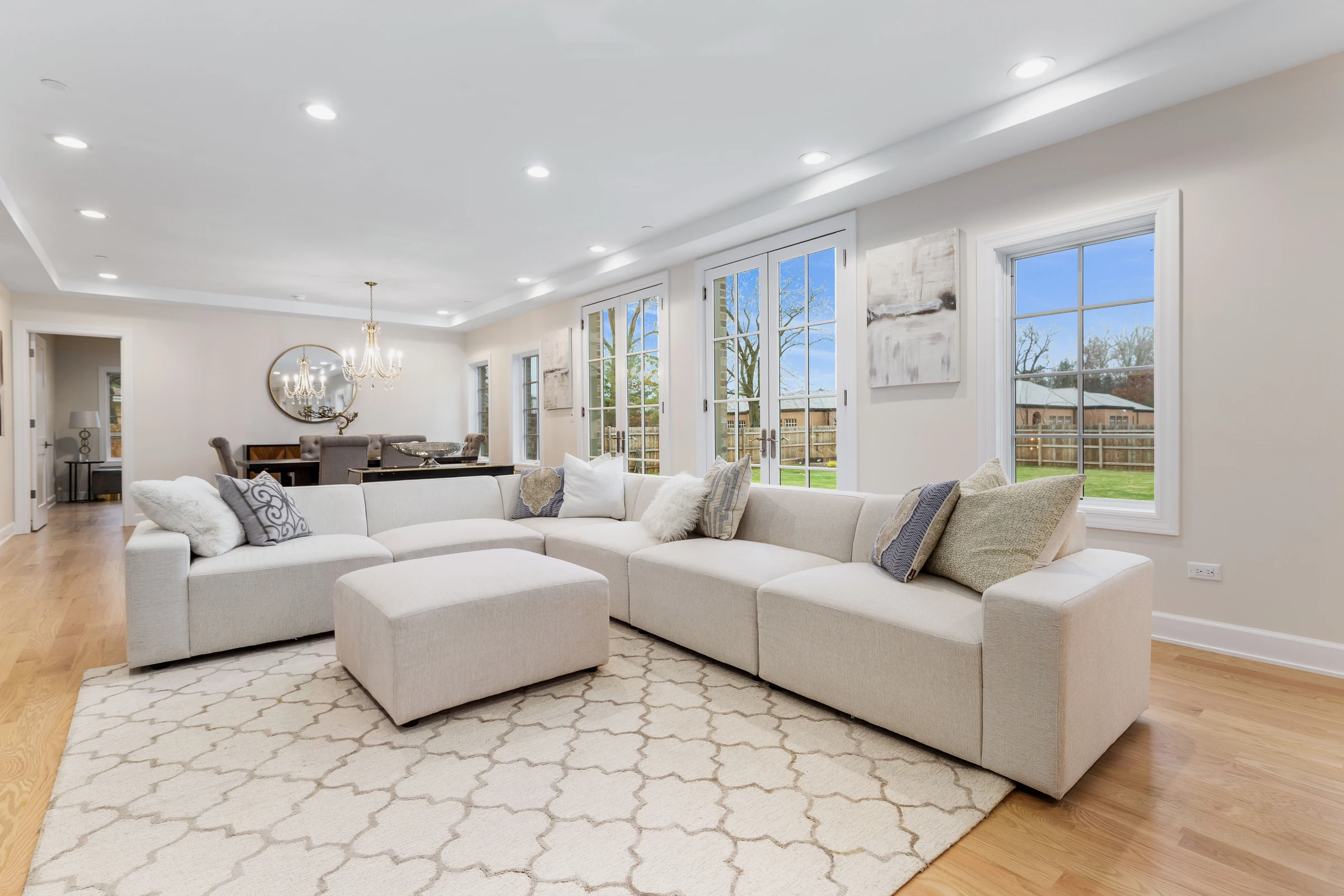 Great room with a sectional sofa, round mirror and tall windows to the garden