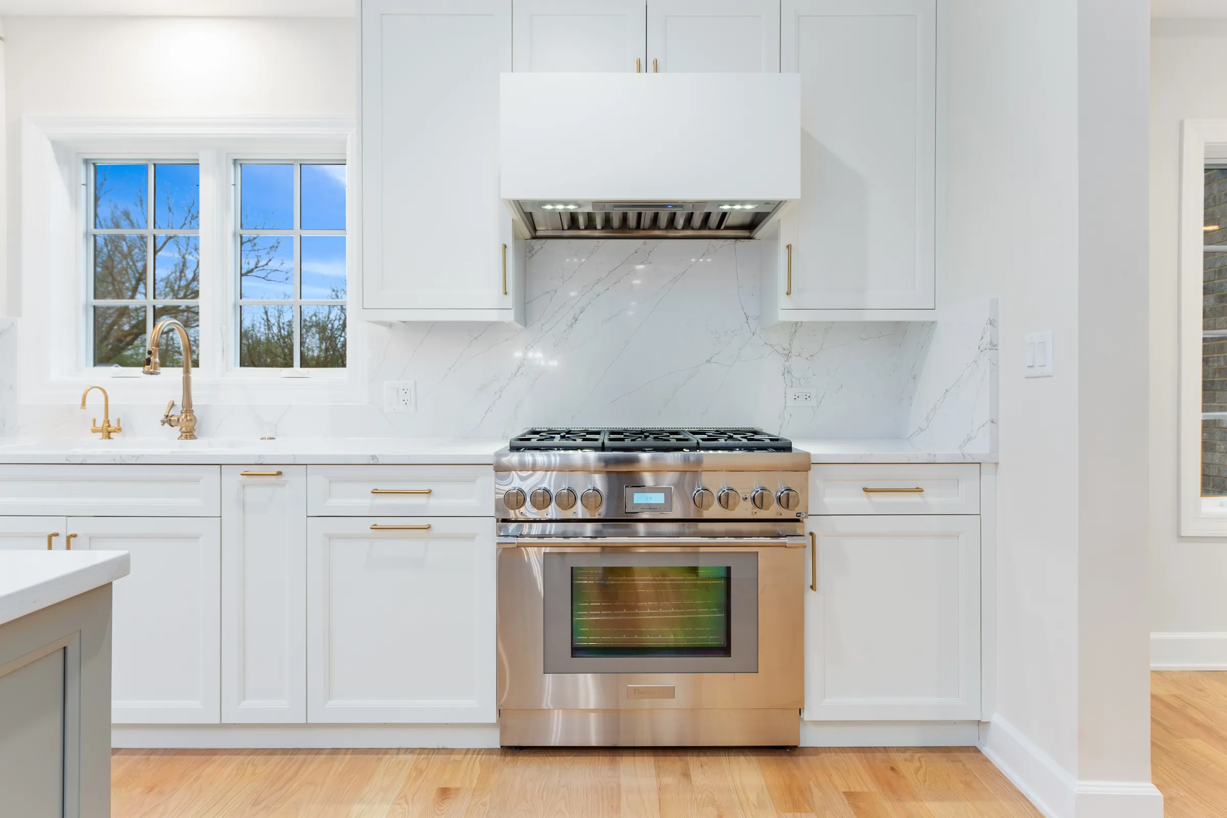 Range with brass hardware beneath a plaster hood and marble backsplash