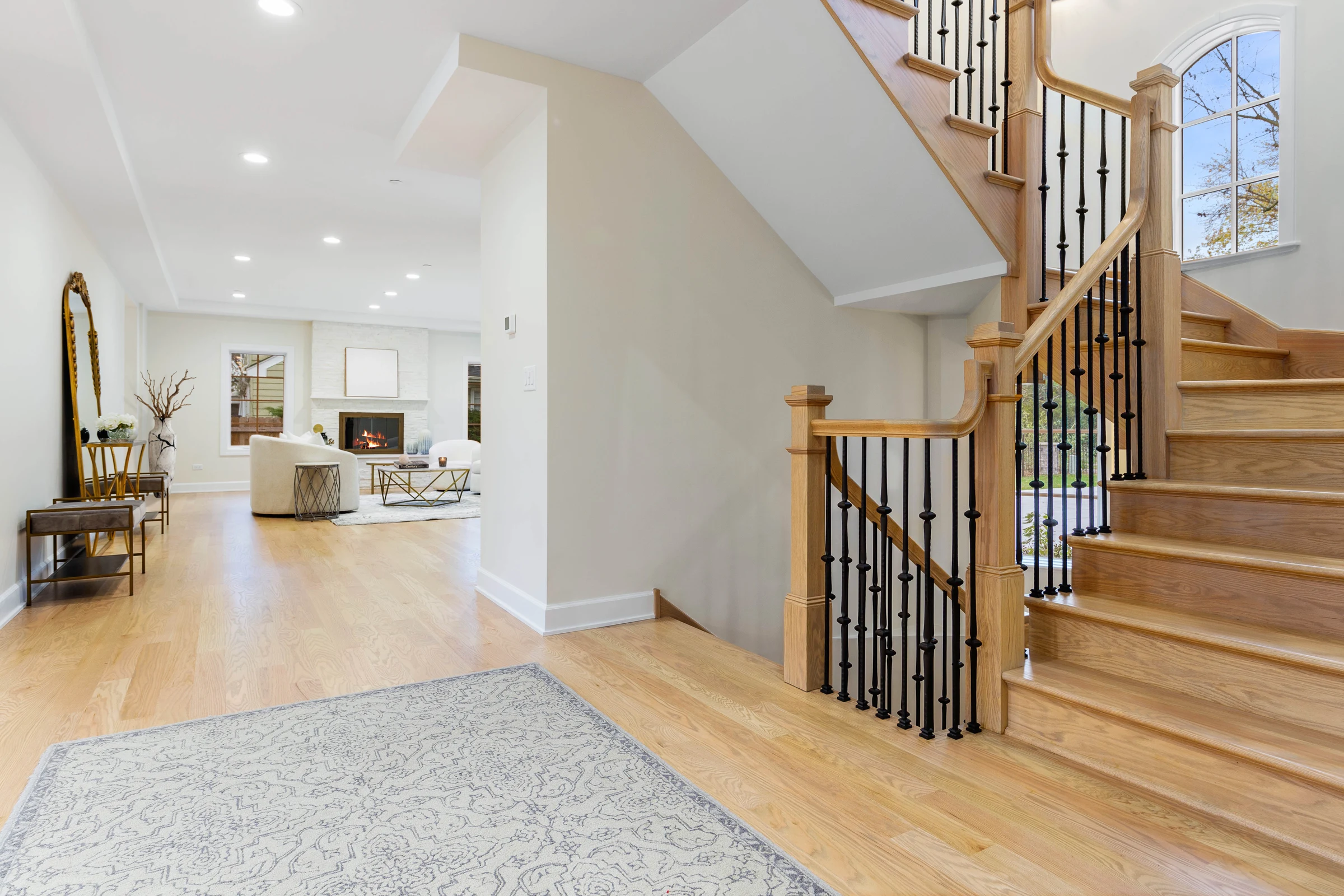 Curved oak staircase rising from the foyer, iron balusters and a gilded mirror